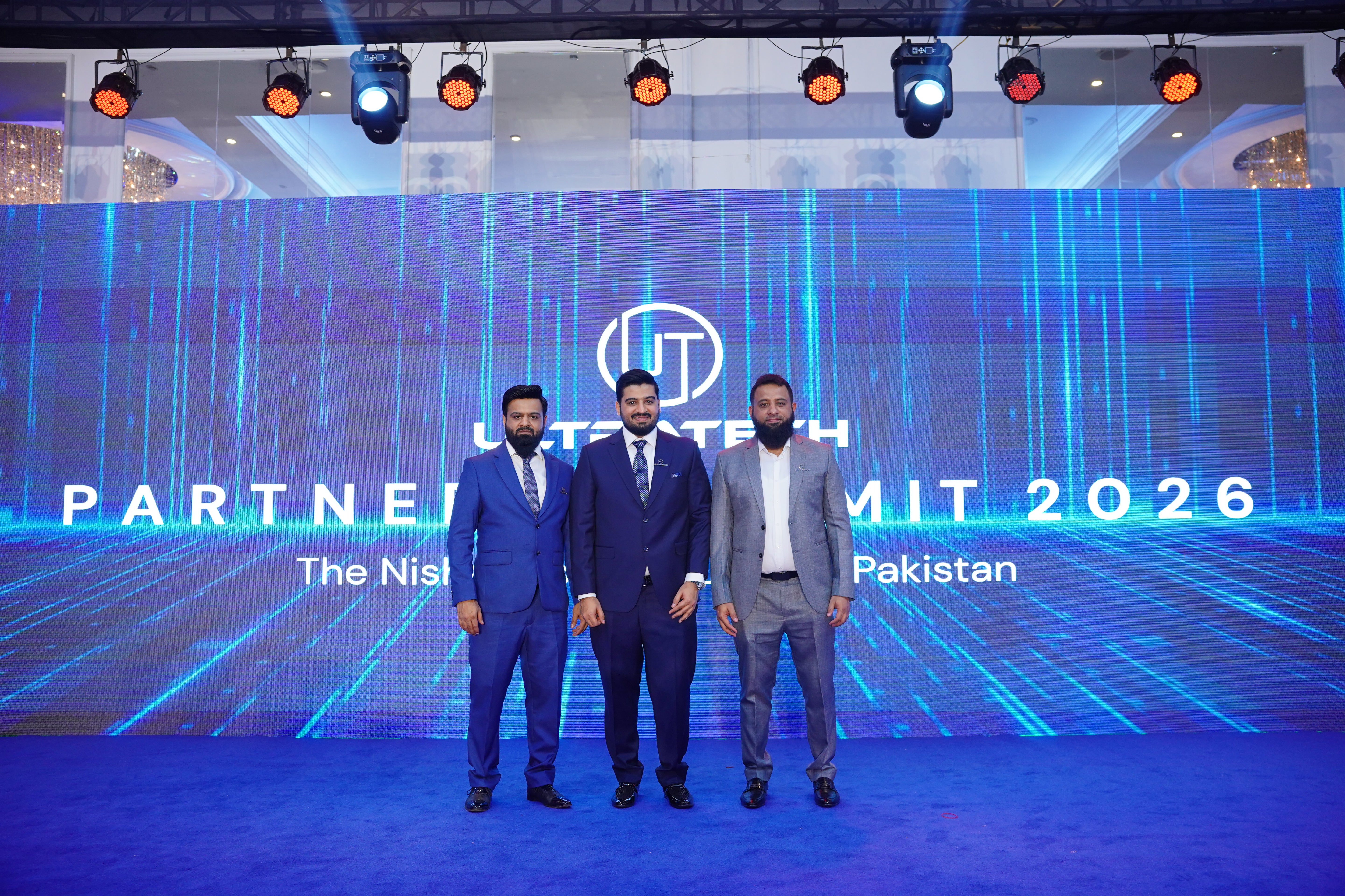 Three men CEO of Ultratech  in suits standing in front of a large screen displaying 'Ultratech PARTNER SUMMIT 2026'.
